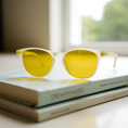 Load image into Gallery viewer, A pair of white-framed blue light blocking glasses placed on top of two books, with yellow lenses, on a window sill.