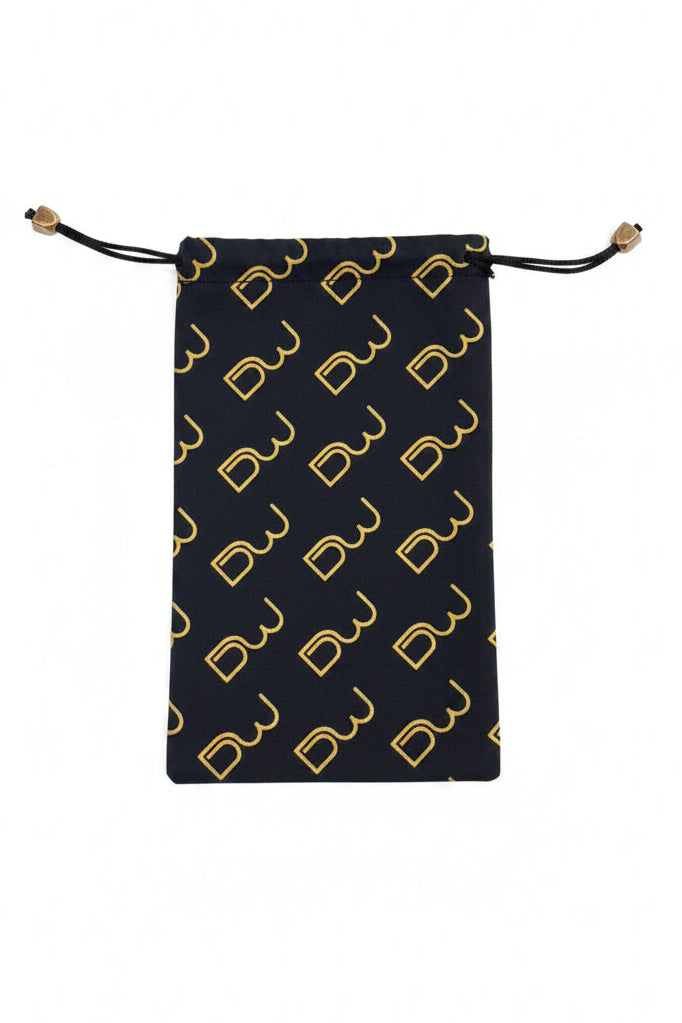 A black drawstring pouch with a repeating gold monogram pattern, laid flat on a textured gray surface.