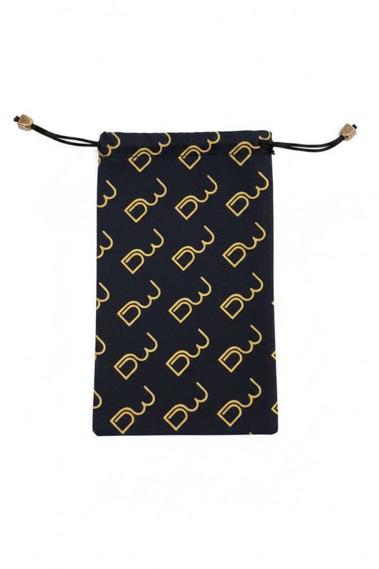 A black drawstring pouch with a repeating gold monogram pattern, laid flat on a textured gray surface.
