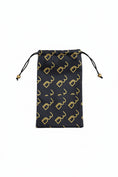 Load image into Gallery viewer, A black drawstring pouch with a repeating gold monogram pattern, held by a hand against a textured gray background.
