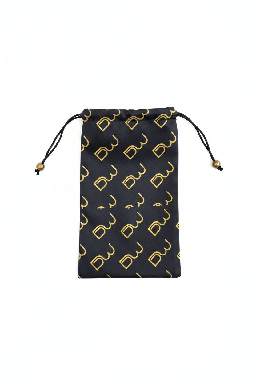 A black drawstring pouch with a repeating gold monogram pattern, held by a hand against a textured gray background.